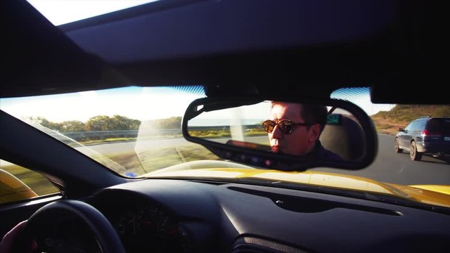 Cabriolet driver's portrait in back mirror. Yellow luxurious car is driving along the Vladivostok road. Beautiful sunny morning