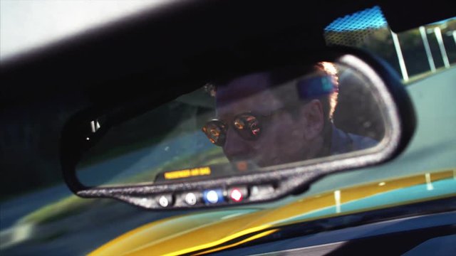 Cabriolet driver's portrait in back mirror. Yellow luxurious car is driving along the Vladivostok road. Beautiful sunny morning