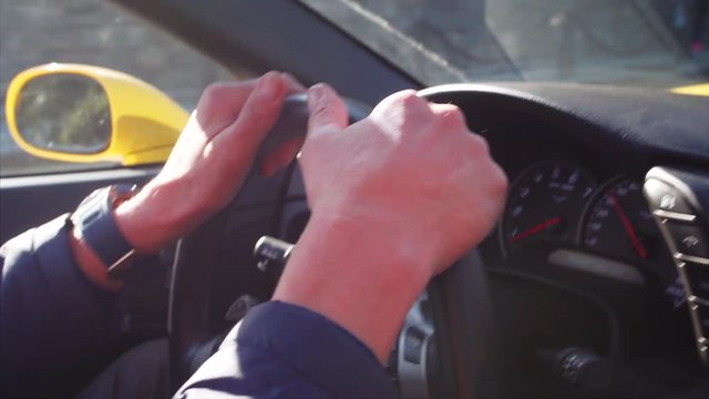 Cabriolet driver's portrait in back mirror. View of his hands on steering wheel. Yellow luxurious car is driving along the Vladivostok road. Russia