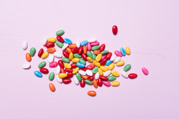 Lots of colorful egg-shaped, sugar coated Easter candy in rainbow colors filled with meringue, chocolate or bubble gum laid out on light pink wooden background