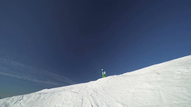 Sportsman snowboarder in bright clothes is riding down fastly on the slope of a mountain at winter sunny day