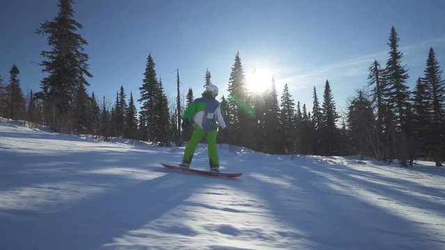 Snowboarder in bright clothes rides down fastly on the slope of a mountain at winter sunny day