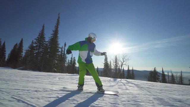 Snowboarder in bright green clothes is riding down fastly on the slope of a mountain at winter sunny day