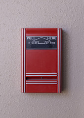 A simple red fire alarm on a white textured wall in a public building