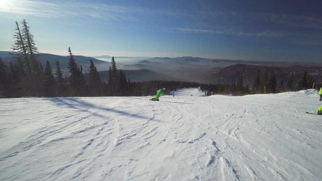 Snowboarder in bright green clothes is riding down fastly on a slope of the mountain at winter sunny day