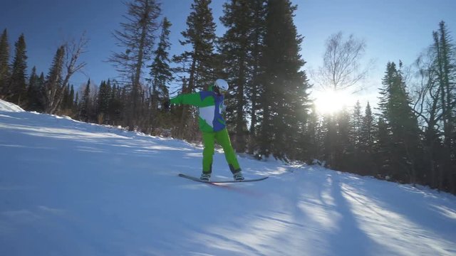 Snowboarder in bright green clothes rides down fastly on a slope of the mountain at sunny winter day