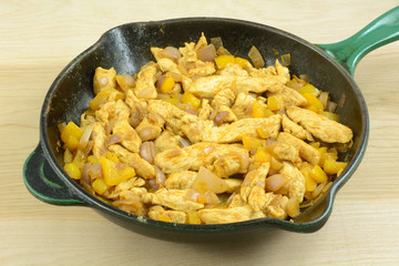 Chicken and yellow bell pepper and shallot onion stir fry with spices in cast iron frying pan skillet