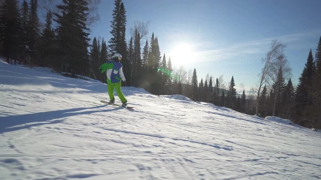 Snowboarder sportsman in bright green clothes is riding down fastly on a slope of the mountain at sunny winter day