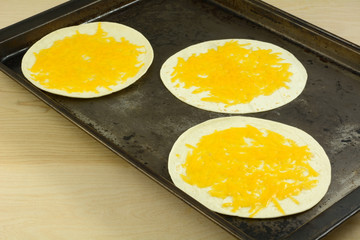 Melted shredded cheddar cheese on tortilla on baking sheet for making fajitas or soft tacos