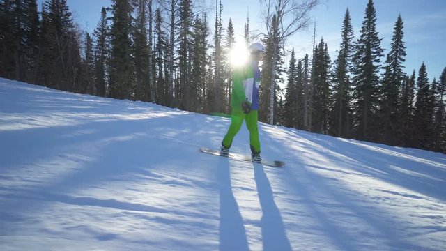 Sportsman on board in bright green clothes is riding down fastly upon a slope of the mountain at sunny winter day