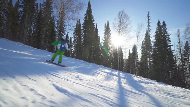 Sportsman on board in bright green clothes rides down fastly upon a slope of the mountain at sunny winter day