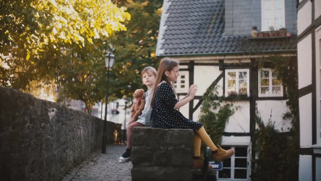 Two European children sit together back to back. Brother and sister have fun on a sunny day. Different personalities 4K.