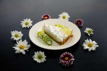 Obraz na płótnie Canvas Lemon pie with lemon shell and flowers in black table