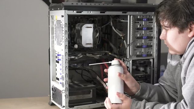 A Computer Geek Boy Cleaning Computer With Compressed Air.Servicing a equipment with Dust-Off Disposable Compressed Gas Duster, canned air..