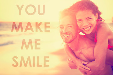Happy smiling couple in love with inspirational quote "YOU MAKE ME SMILE" for lovers or valentines day socia media inspiration. Multiracial Asian caucasian couple on beach at sunset laughing.