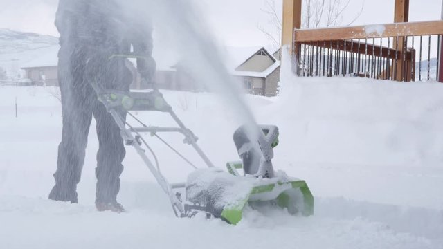 A dolly shot of a man snowblowing the driveway after storm