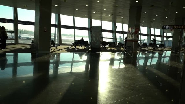 airport terminal interior, people travellers passengers silhouettes waiting in a lounge, hall view, beautiful background with sunshine, dolly shot from escalator