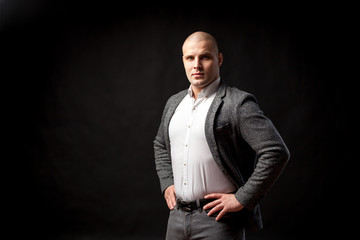 A  bald man businessman  in a white shirt, gray suit  stands in a confident pose, straightening his shoulders on a black isolated background