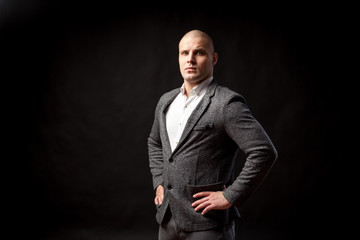 Obraz premium A young man manager in a white shirt, gray suit looks seriously and holds his hands at the waist on a black isolated background