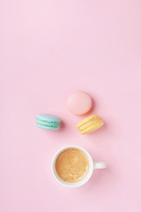 Morning cup of coffee and colorful cake macaron on pastel pink background top view. Cozy breakfast. Fashion flat lay. Sweet macaroons.