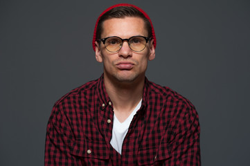 Portrait of young stylish thoughtful hipster guy looking at the camera on gray background