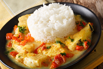 Stew fish with sauce of cilantro, onions, tomatoes, bell peppers and coconut milk with garnish of rice. Horizontal