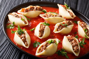 Italian cuisine: onchiglioni pasta stuffed with ground beef with greens in tomato sauce close-up on plate. horizontal