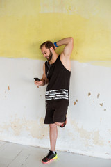 a sports man is staying near the wall and holding smartphone in his hand. Chatting on the phone and listening music.