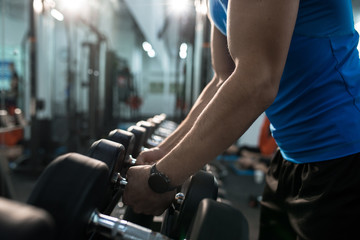 Fototapeta na wymiar Side view close up of strong male hands picking up dumbbells from equipment stand in modern gym, copy space