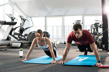 Fototapeta premium Portrait of young sports couple pushing up on mats in modern gym, copy space