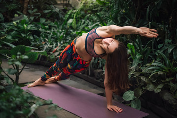 Attractive caucasian female yoga instructor stretching on mat at greenhouse