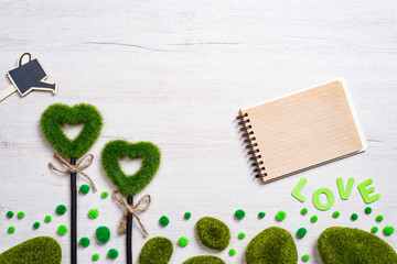 Two green grassy hearts, notebook and watering can on a white wooden background. The concept of Valentine Day