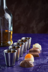 Fototapeta na wymiar set of five servings of cognac with a variety of chocolates on a dark purple background