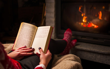 Female reading a book by the fireplace