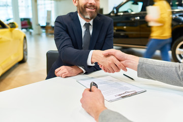Close up of  client shaking hands with sales manager after signing purchase contract to buy new car in showroom
