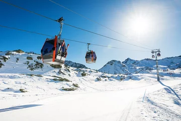 Tuinposter skiliftgondels tegen blauwe hemel over helling bij skitoevlucht op zonnige de winterdag bij de Alpen van Italië © ronstik