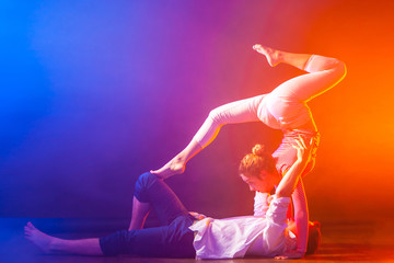 A girl and a man dance an acrobatic dance. The girl is making a twine. The girl is standing on her hands.