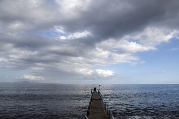 Wooden port pier with fisherman silhouette on the end, wild ocean with waves, Funchal, Madeira, Portugal