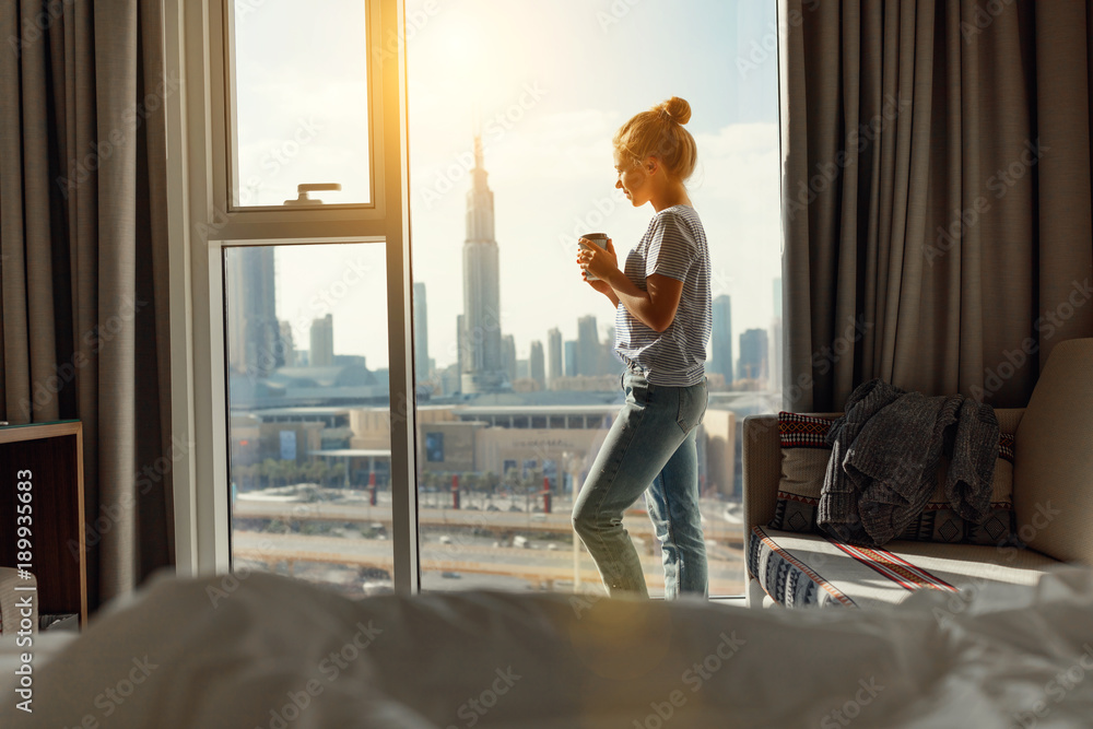 Poster happy young woman drinks coffee in morning at window