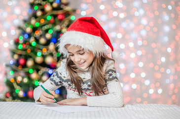smiling girl in red christmas hat writes letter to Santa Claus. Space for text