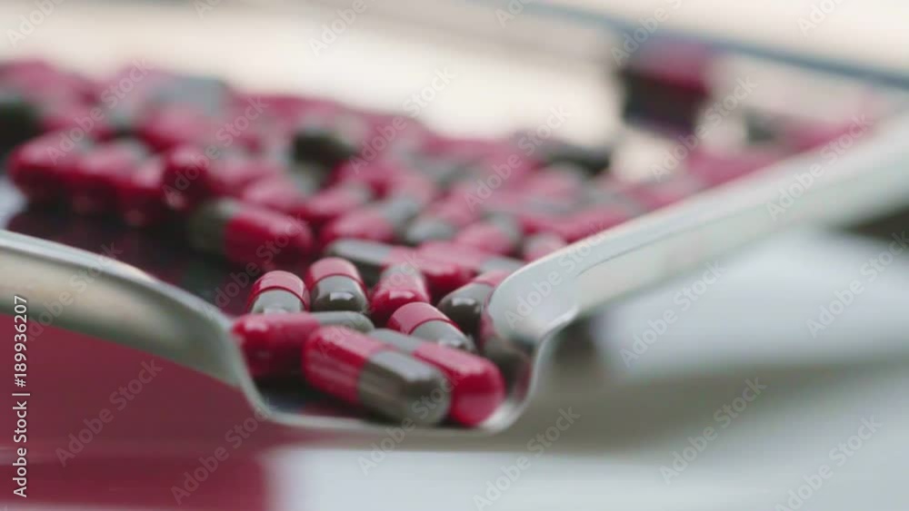 Wall mural Many of red and gray capsules pills flow and fall from the stainless steel medicine tray.