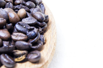 close up of roasted coffee beans on a wood spoon with white background with space for text.