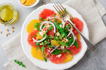 Citrus vitamin salad. Orange, grapefruit, ricotta cheese, pine nuts, red onions and arugula with olive oil in ceramic plate on gray concrete or stone old background.Top view. 