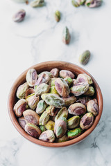 Pistachios in wooden bowl on marble background with copy space 