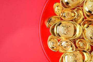 Top view group of golden ingots on red tray at red background.Chinese new year concept,leave space for adding text.Chinese Language on ingot mean wealthy.