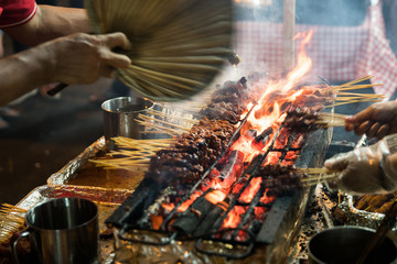 Meat skewers cook over hot coals in Singapore's Satay Street food market - obrazy, fototapety, plakaty