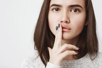 Fototapeta premium Close up portrait of attractive european female with concerned and thoughtful expression holding fingers on lips, over white background. Girl thinks about fight they had with her boyfriend and regrets