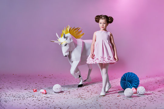 Romantic little girl in beautiful pink dress. Origami and minimalism. Fashion children. Designer collection. White big unicorn origami made of paper.