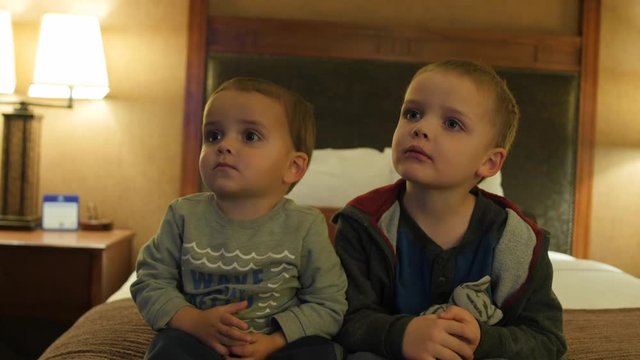 Cute little boys watching TV in a hotel room at night