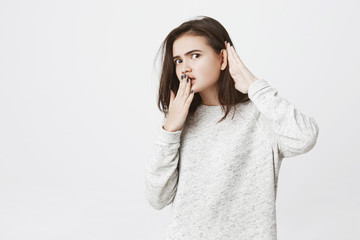Portrait of young female employee eavesdropping or overhearing something, holding hands near mouth...